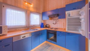 Una cocina compacta con armarios azules, lavavajillas, horno y refrigerador.