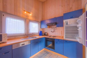 Una cocina compacta con armarios azules, lavavajillas, horno y refrigerador.