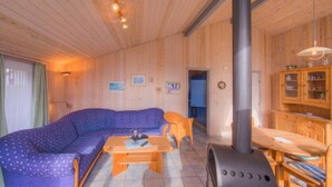 Interior de una cabaña de madera con sofá, mesa y una estufa grande.