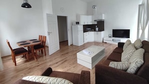 Uma sala de estar moderna com um sofá marrom, uma mesa de centro, uma mesa de jantar com cadeiras, uma área de cozinha com armários e uma televisão.