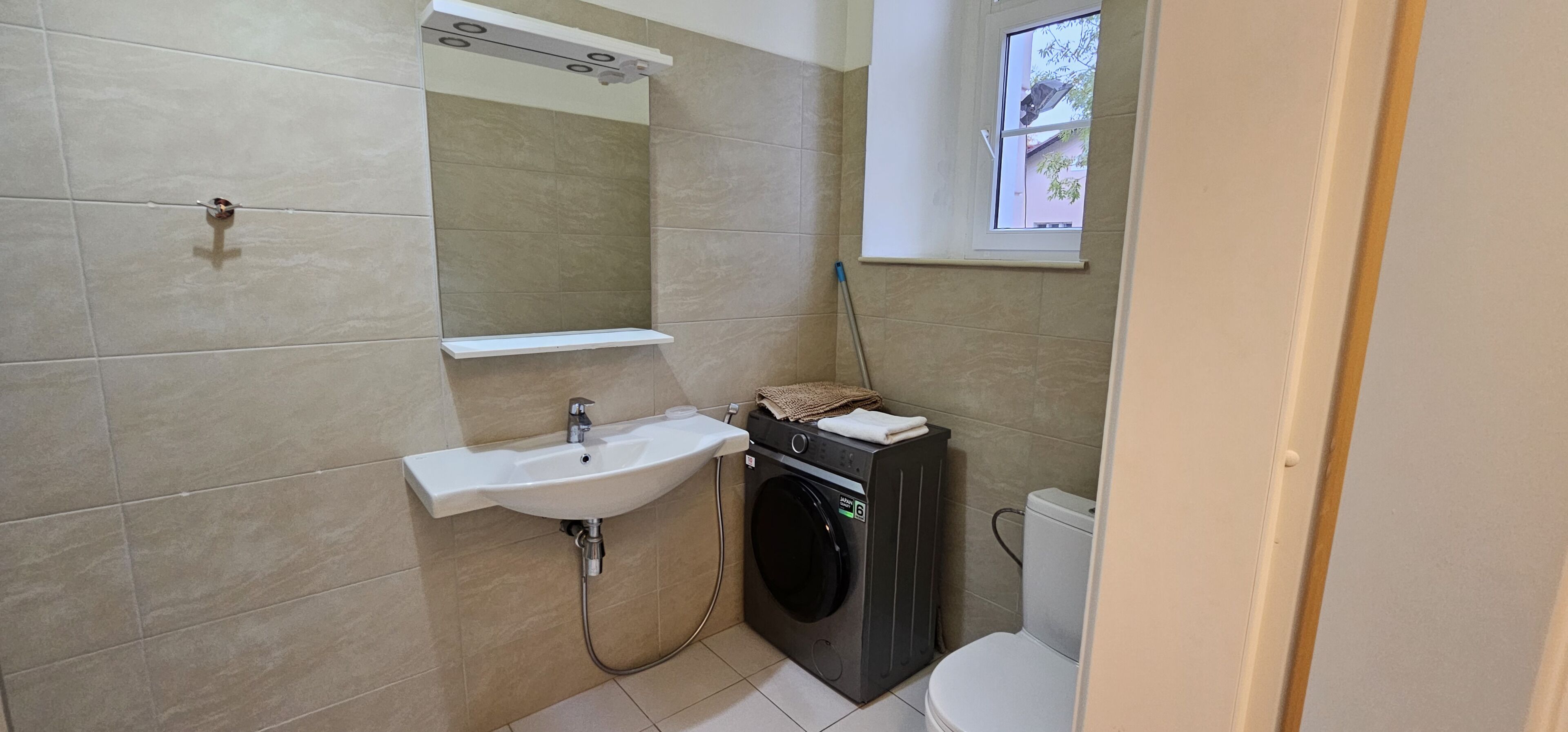 A bathroom with a sink, mirror, washing machine, and toilet.