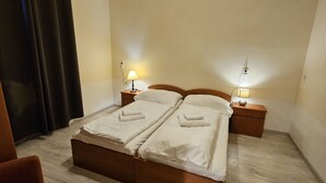 Quarto de hotel com uma cama de casal, duas mesas de cabeceira com luminárias, uma cabeceira de madeira e uma cortina escura.