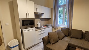 Um espaço compacto com cozinha americana, sofá com almofadas e janela com cortinas.