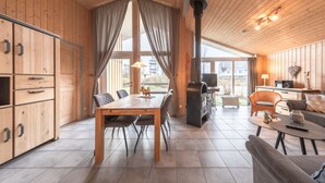 A spacious living area with a wooden ceiling, a dining table, and a kitchen area with cabinets and a stove. - Ferienhaus im Skandinavischen Stil (Rechlin)