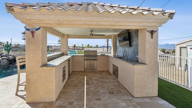 An outdoor kitchen with a stone floor, a grill, and a pool in the background. - Havasu Hacienda Private Pool! (Lake Havasu City)