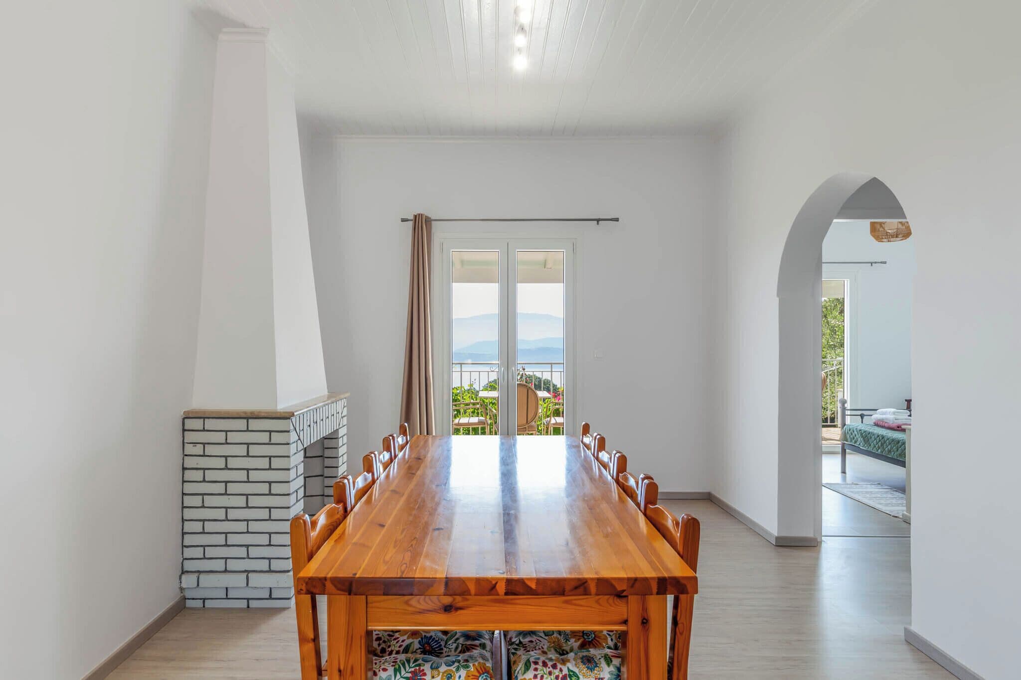 Un comedor con una larga mesa de madera, sillas, una chimenea de ladrillo y vistas al balcón exterior a través de un ventanal.