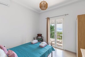 A bedroom with a bed, a chair, a balcony with a table, and a view of the outdoors. - Villa Marialetta (Corfu)