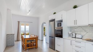 A modern kitchen with white cabinets, stainless steel appliances, and a dining area with a wooden table and chairs.