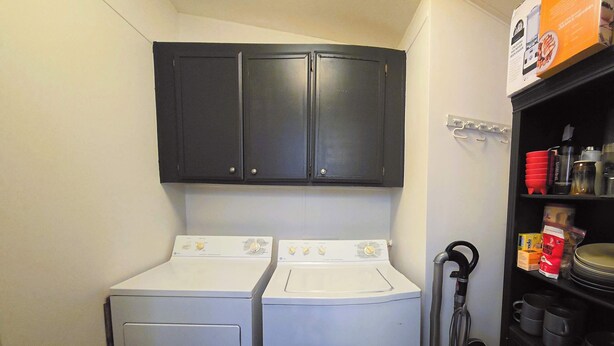 A laundry room with two front-loading washing machines and a dryer, a black cabinet above, and a shelf with kitchenware and cleaning supplies. - Oak Creek Viewpoint The Views! (Sedona)