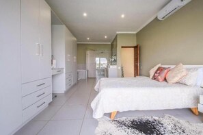 Ein Schlafzimmer mit Bett, Kleiderschrank, Schreibtisch und einem Badezimmer im Hintergrund.