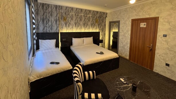 A hotel room with two beds, a mirror, a wooden door, and a small table. - PENDİK SUİT OTEL (Istanbul)