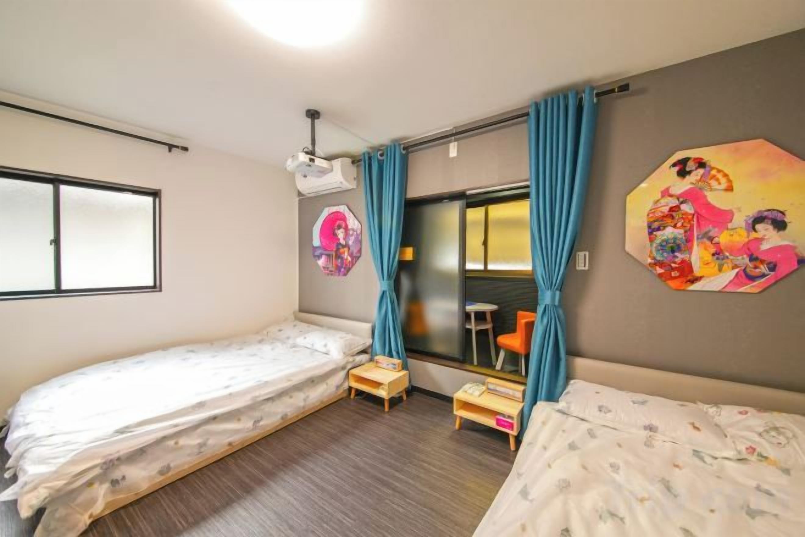 A room with two single beds, a small table, a window, and a wall with a painting.