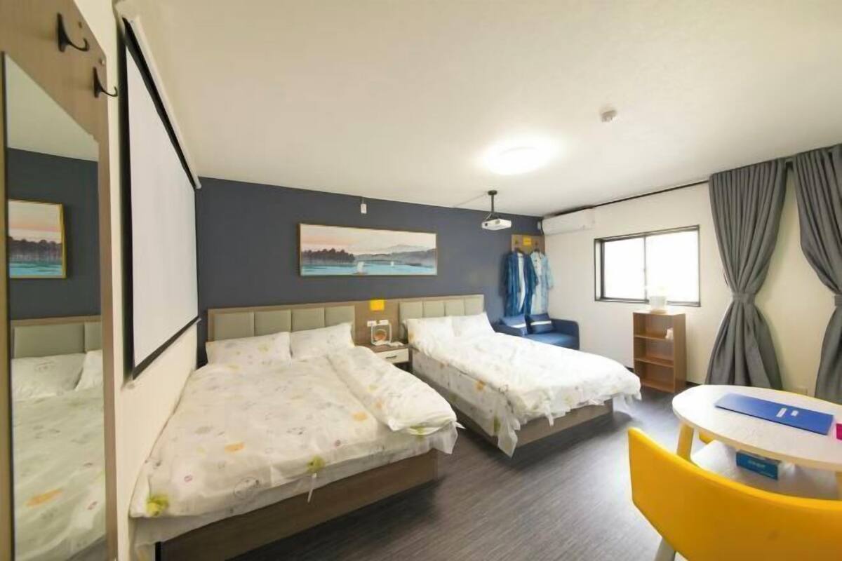Une chambre d’hôtel avec deux lits, une petite table, une chaise, une fenêtre avec des rideaux et un tableau au mur.