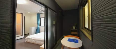 A narrow hotel room with a bed, a small table, and a chair.