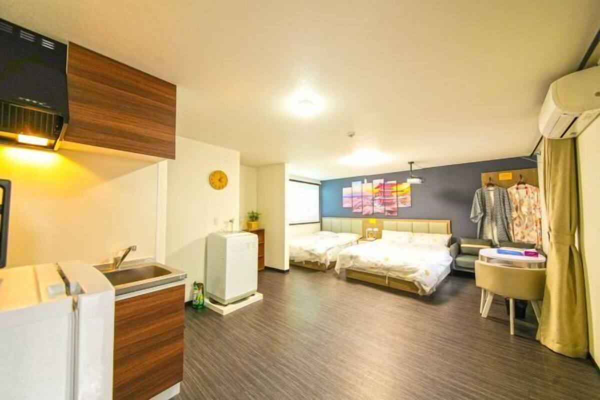 Une chambre d’hôtel équipée d’une kitchenette, de deux lits, d’un petit coin salon et d’un mur orné d’une œuvre d’art colorée.