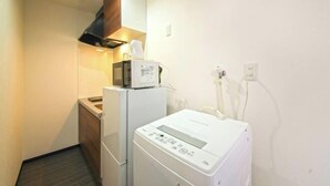 A compact kitchenette with a microwave, a small refrigerator, and a washing machine. - Osaka Blue House / Disposable Bedding / Four Stops Within an Eight-Minute Walk (Osaka)