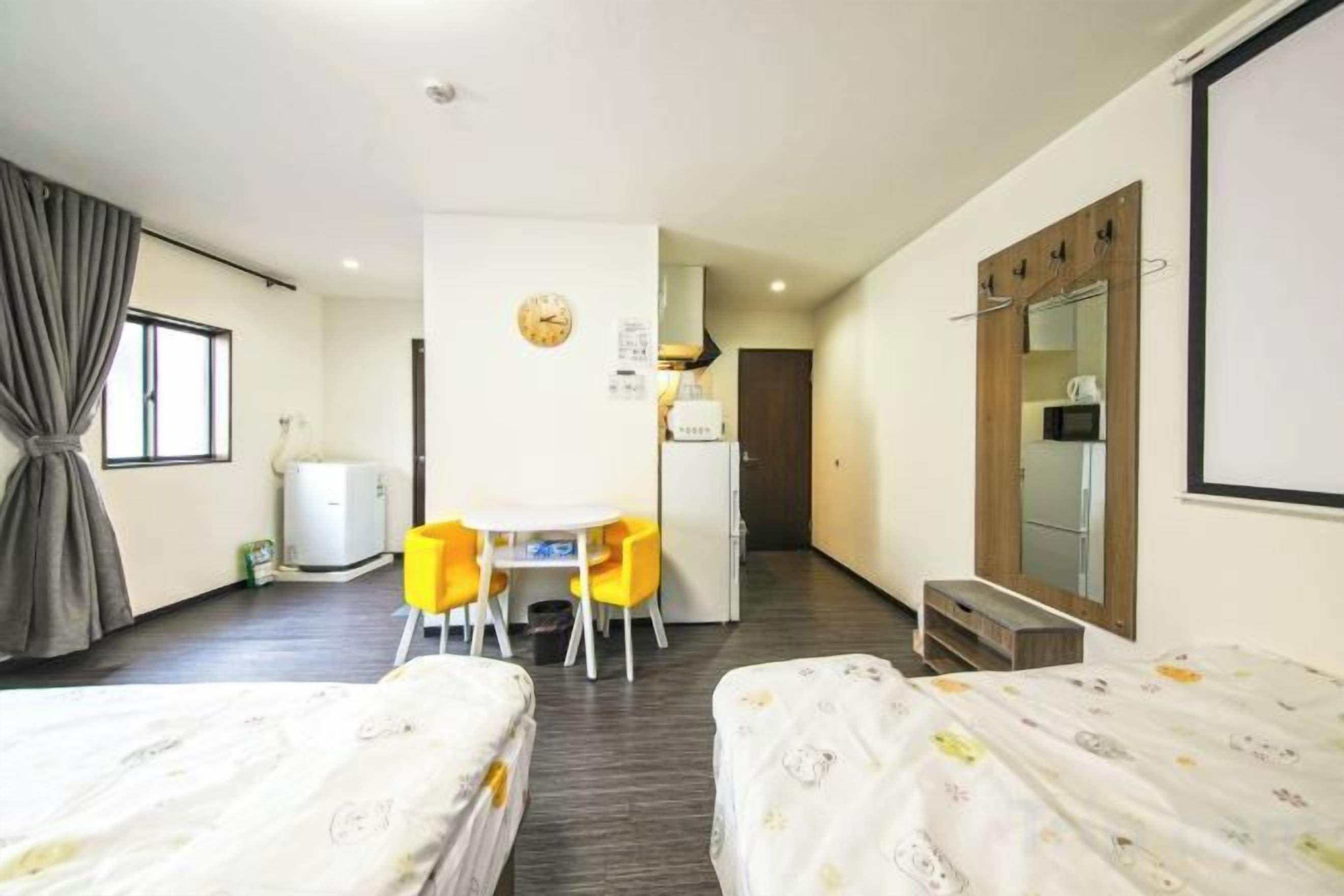 A hotel room with two beds, a desk with chairs, a mirror, and a window with curtains.