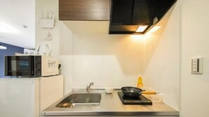 A compact kitchen with a microwave, sink, and a black frying pan on the counter. - Osaka Blue House / Disposable Bedding / Four Stops Within an Eight-Minute Walk (Osaka)