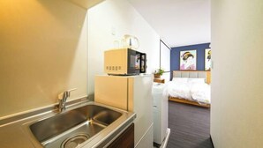 A compact hotel room with a kitchenette, a bed, and a small bathroom. - Osaka Blue House / Disposable Bedding / Four Stops Within an Eight-Minute Walk (Osaka)