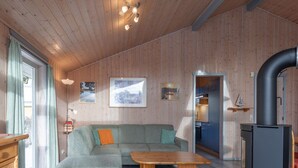 Un salon chaleureux avec un canapé d’angle, une table basse en bois et un coin cuisine visible à travers une porte ouverte.