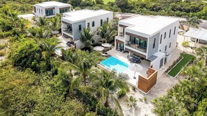 Una casa moderna de dos pisos con piscina, rodeada de exuberante vegetación y un campo de golf al fondo.