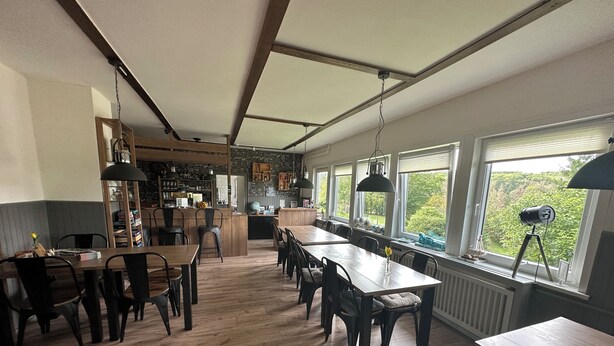 A spacious kitchen with wooden flooring, a central island, and large windows offering a view of greenery. - World Lodge with unique, city-inspired rooms, located by the forest (Altenau)
