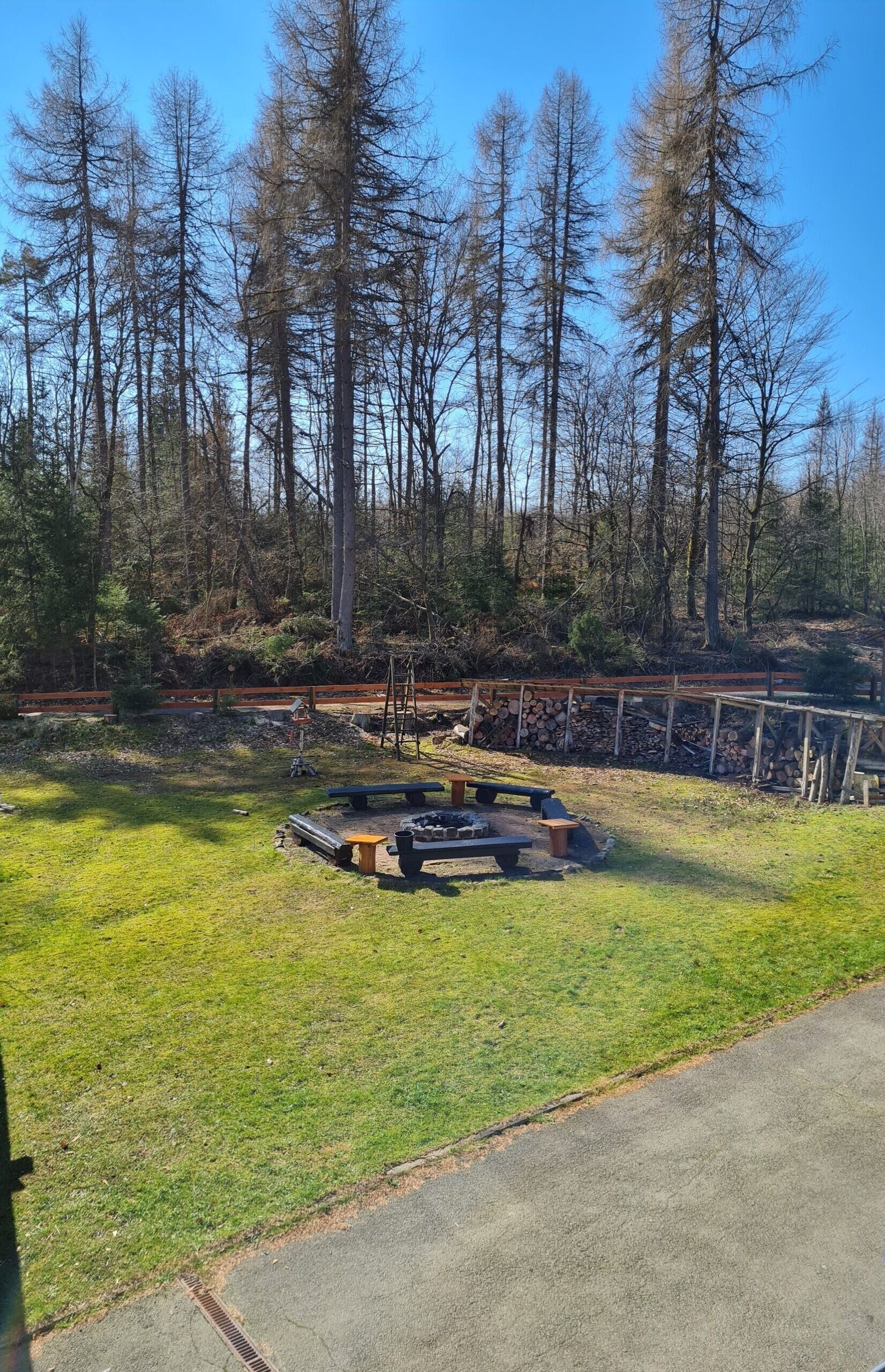 A grassy area with a concrete path, a wooden bench, and a metal fire pit.