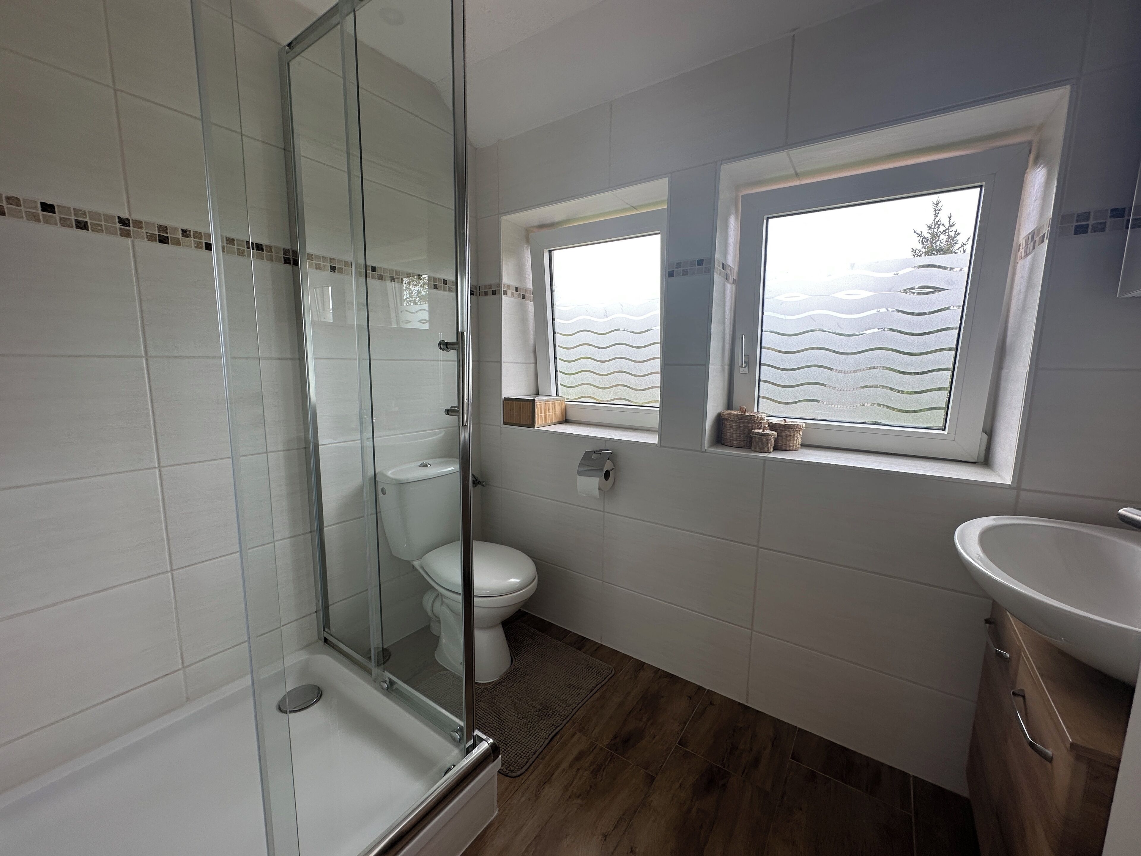A bathroom with a glass shower enclosure, a toilet, a window with a view, and a sink.