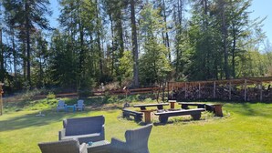 An outdoor seating area with wicker furniture and picnic tables, surrounded by a wooden fence and a stack of firewood. - World Lodge with unique, city-inspired rooms, located by the forest (Altenau)