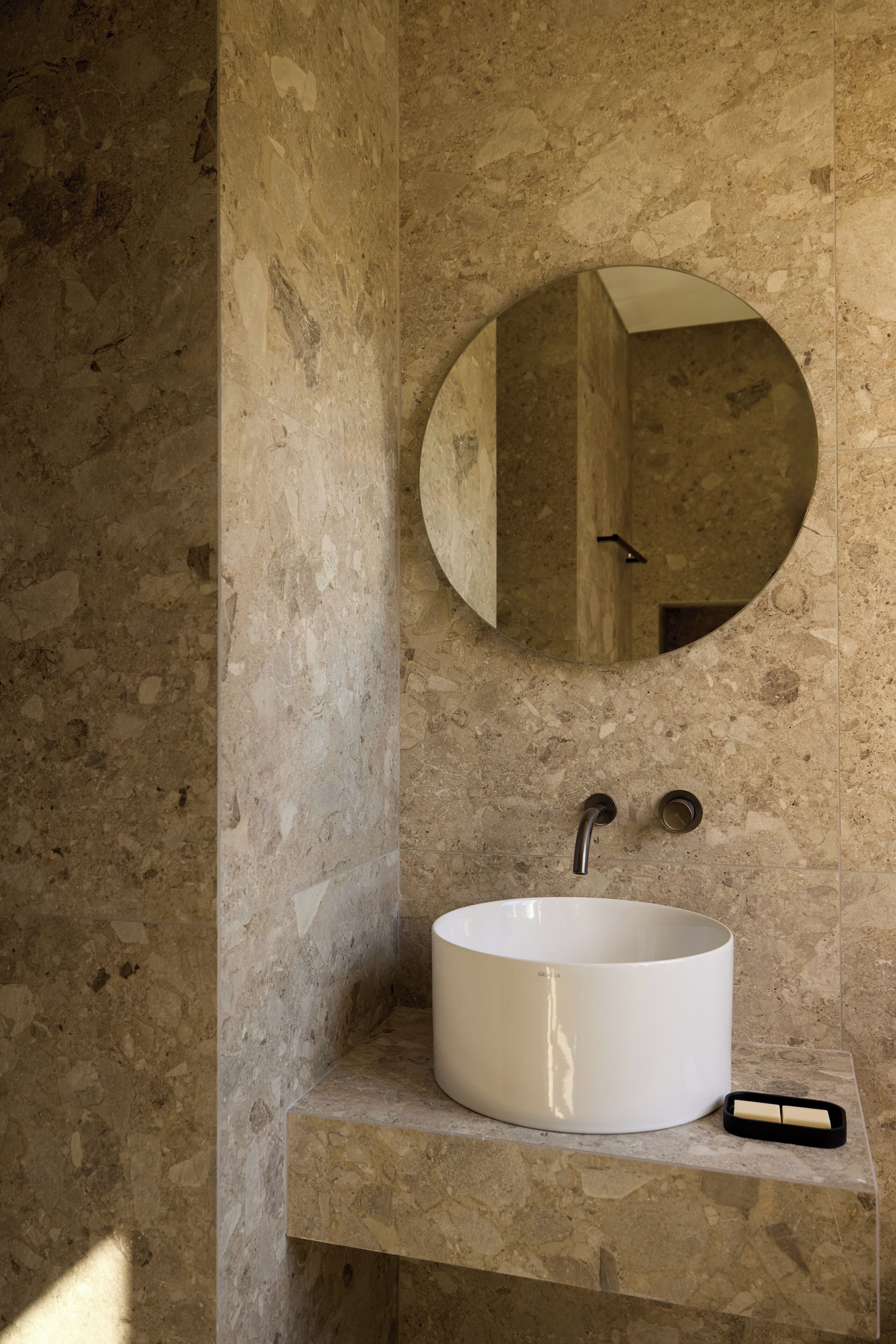 A bathroom with a round mirror, a white sink, and a marble countertop.
