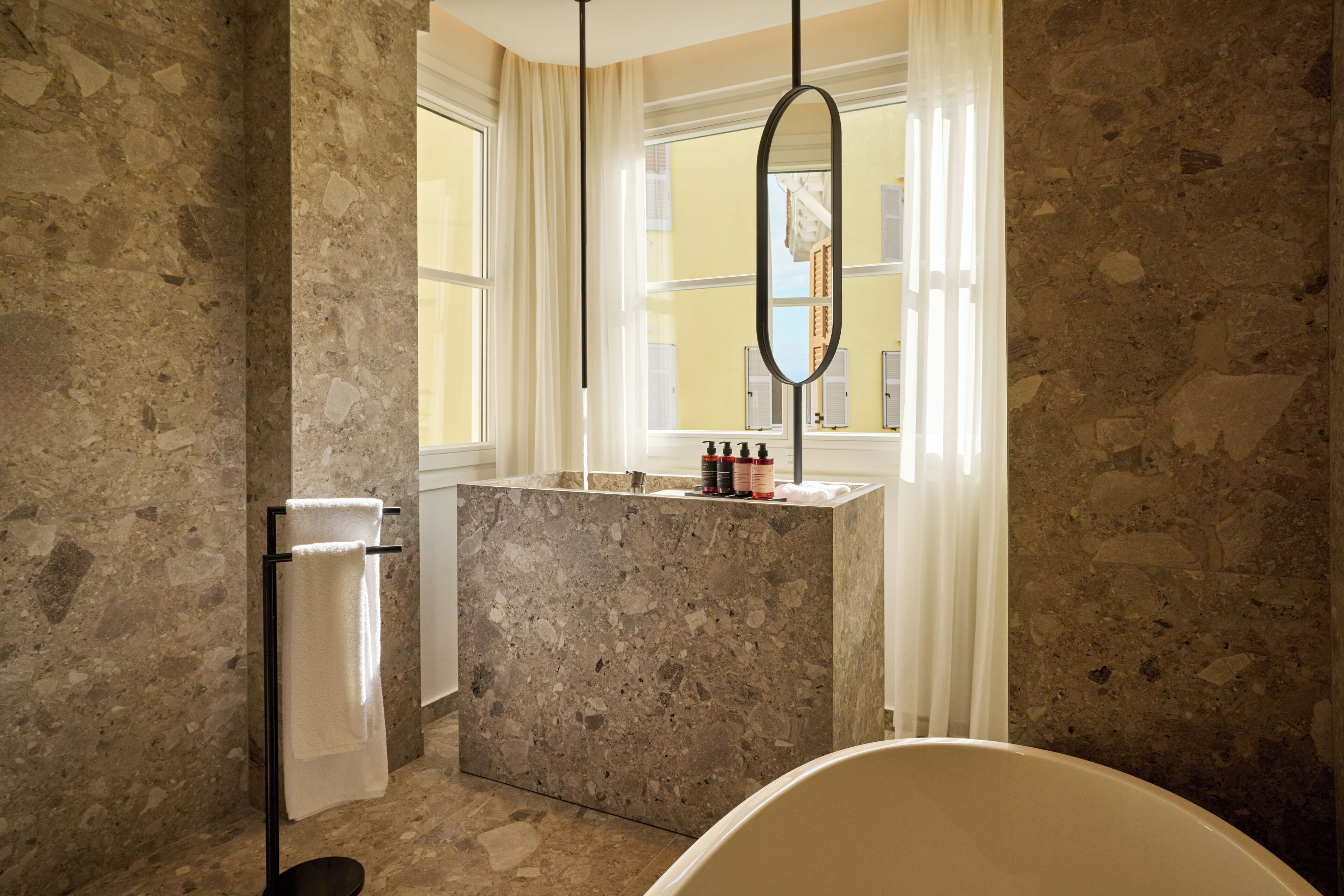 Un bagno con parete in marmo, una vasca da bagno, un porta asciugamani e una finestra con tende.