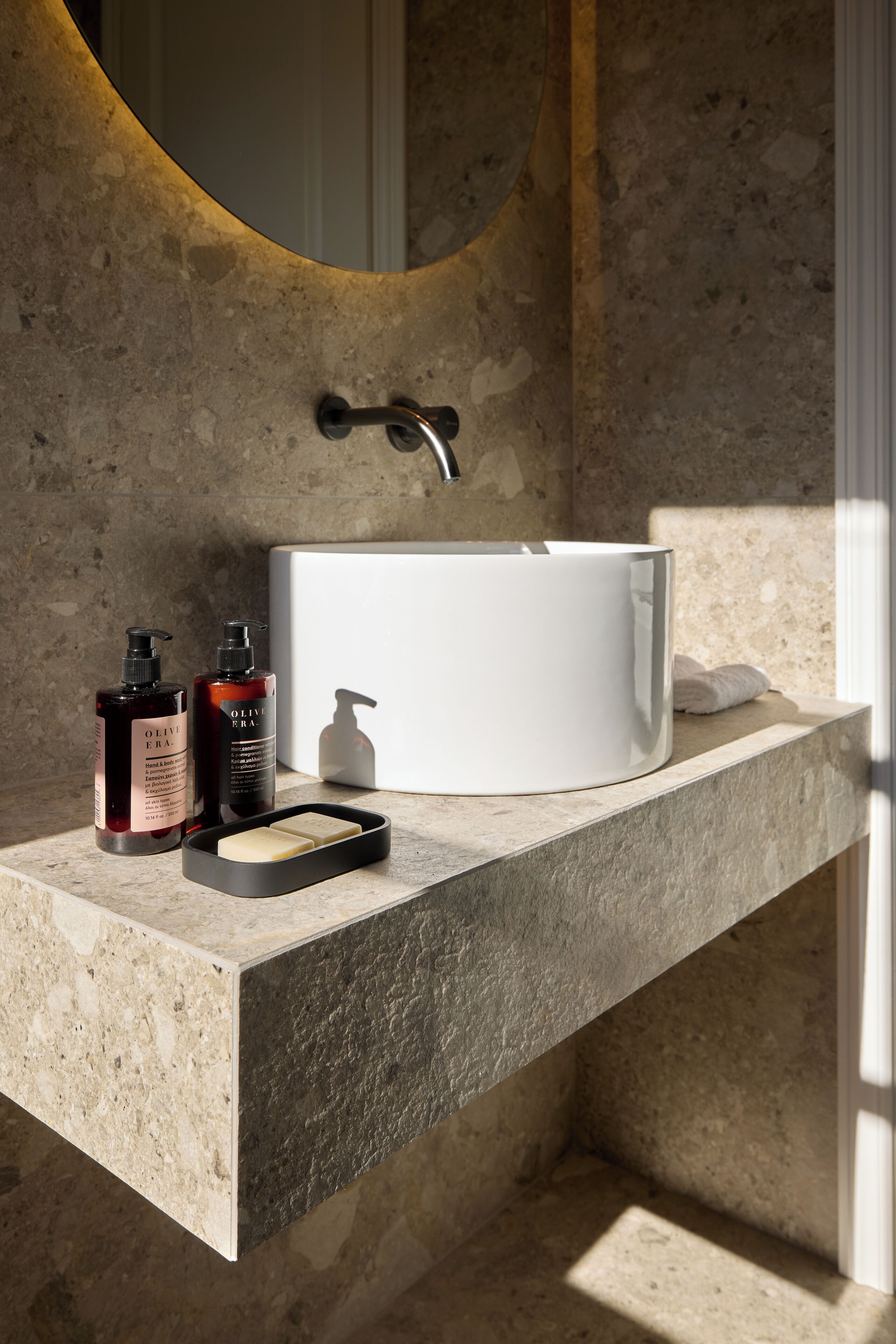 A bathroom with a marble countertop, a white sink, and two bottles of olive oil.
