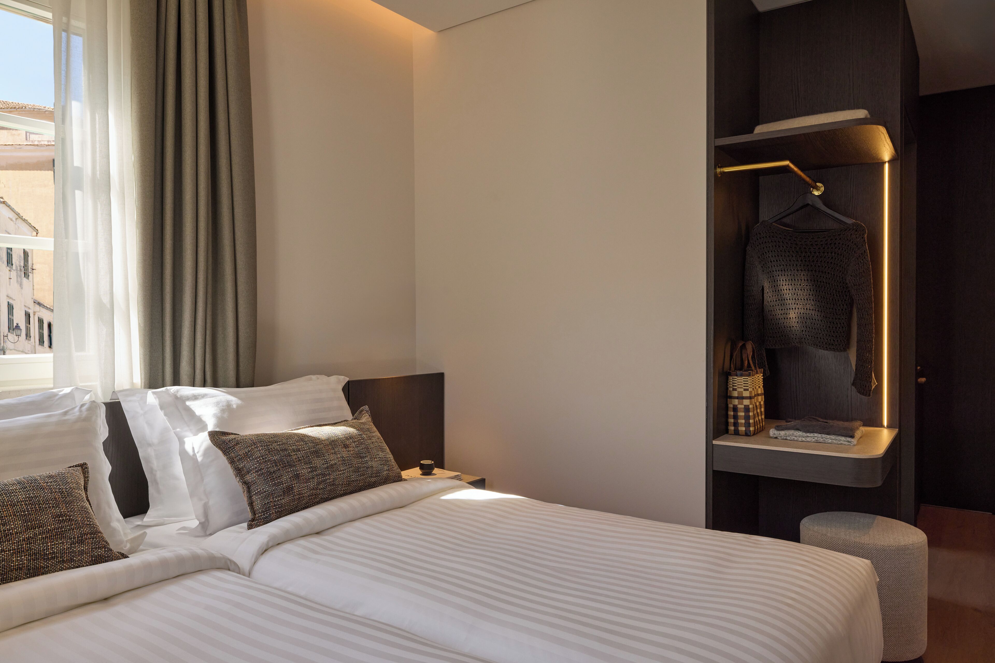 Una habitación de hotel moderna con una cama bien hecha, una mesita de noche con lámpara y vistas a la ciudad por la ventana.