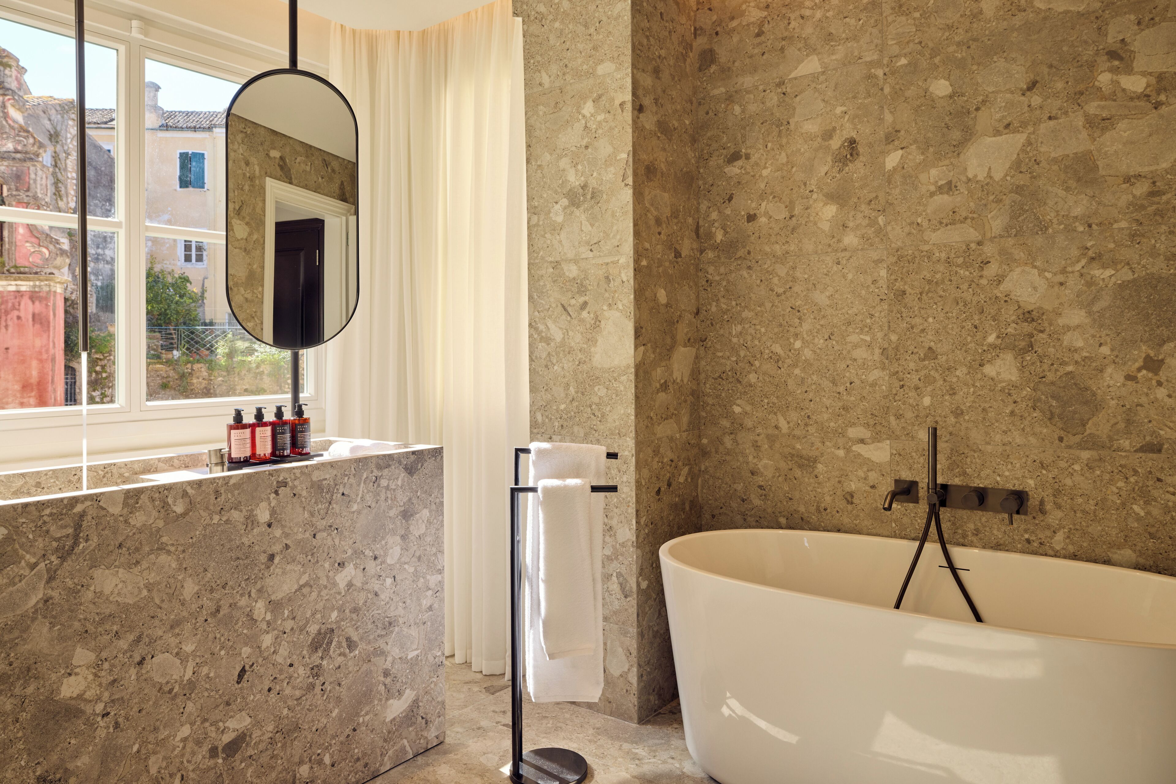 A bathroom with a freestanding bathtub, a marble countertop, a window with curtains, and a mirror.