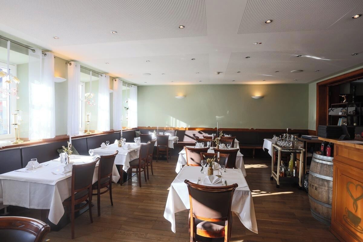 A restaurant with multiple tables and chairs, wooden flooring, and a bar area with a barrel.