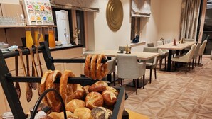 A breakfast buffet with various pastries and bread, a coffee machine, and seating arrangements in a modern dining area. - Hotel Lutz (Rain)