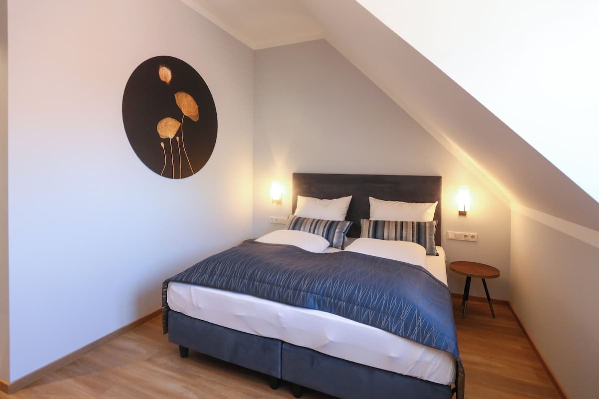 Un dormitorio con una cama, dos mesitas de noche, una obra de arte en la pared y un techo inclinado.