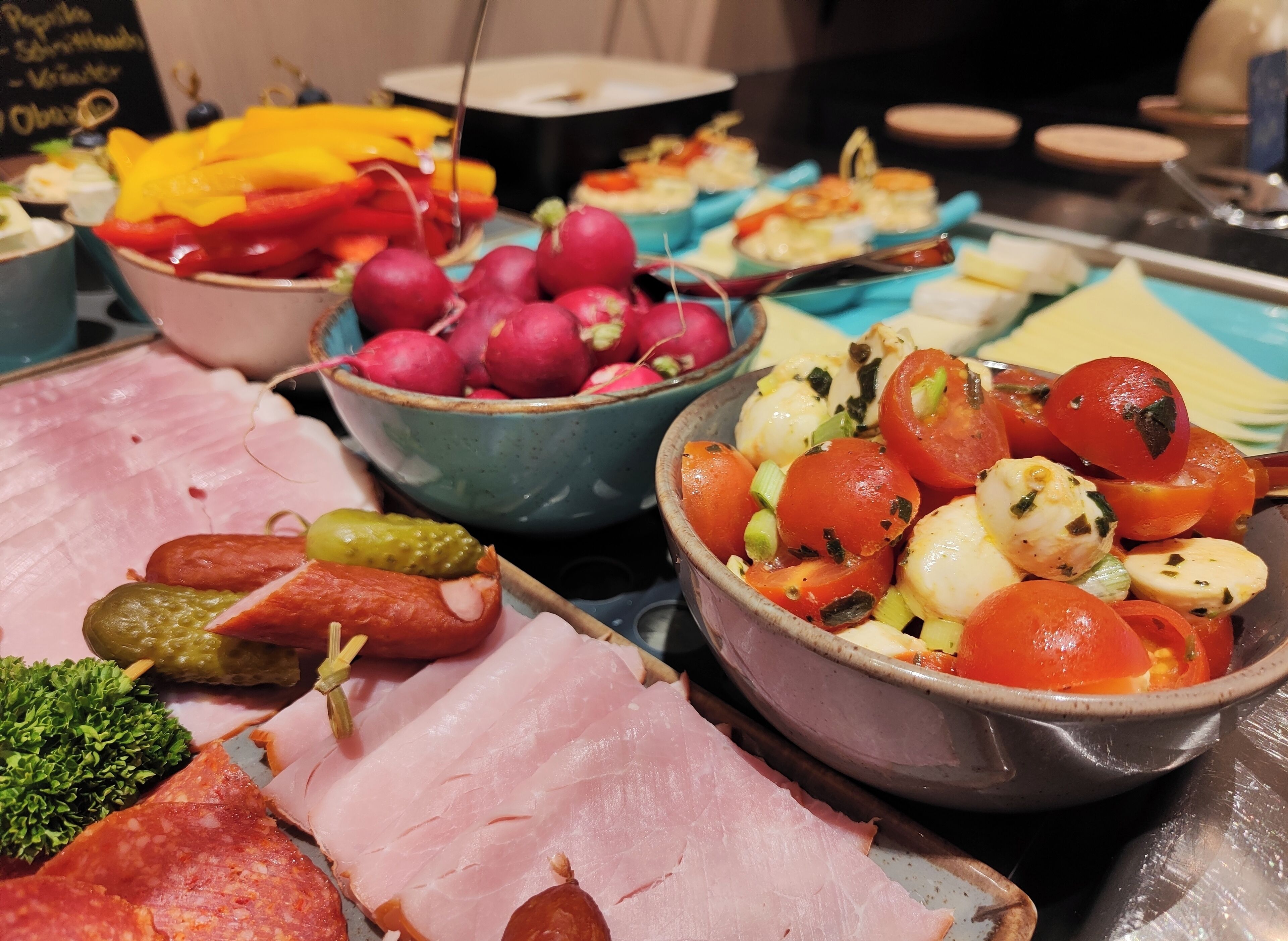 Ein reichhaltiges Buffet mit verschiedenen Speisen, darunter Aufschnitt, eingelegtes Gemüse, Radieschen und eine Schüssel mit Tomaten und Oliven.