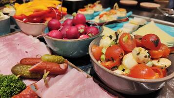 Ein reichhaltiges Buffet mit verschiedenen Speisen, darunter Aufschnitt, eingelegtes Gemüse, Radieschen und eine Schüssel mit Tomaten und Oliven.