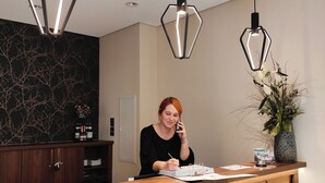 A reception desk with a wooden finish and a modern pendant light fixture. - Hotel Lutz (Rain)