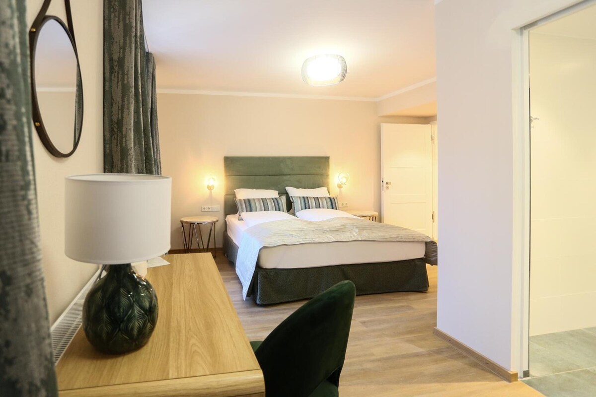 A hotel room with a bed, bedside tables, a lamp, and a chair.