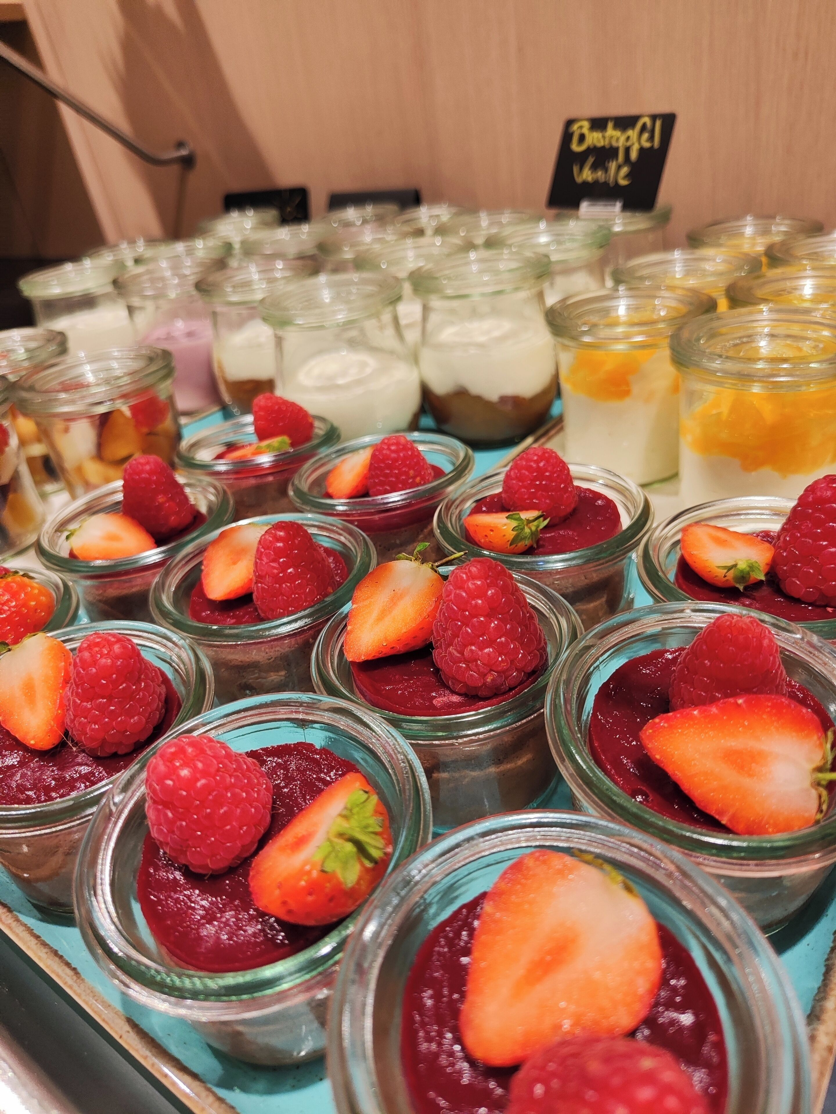 A display of various desserts in glass jars, including strawberry and raspberry toppings.