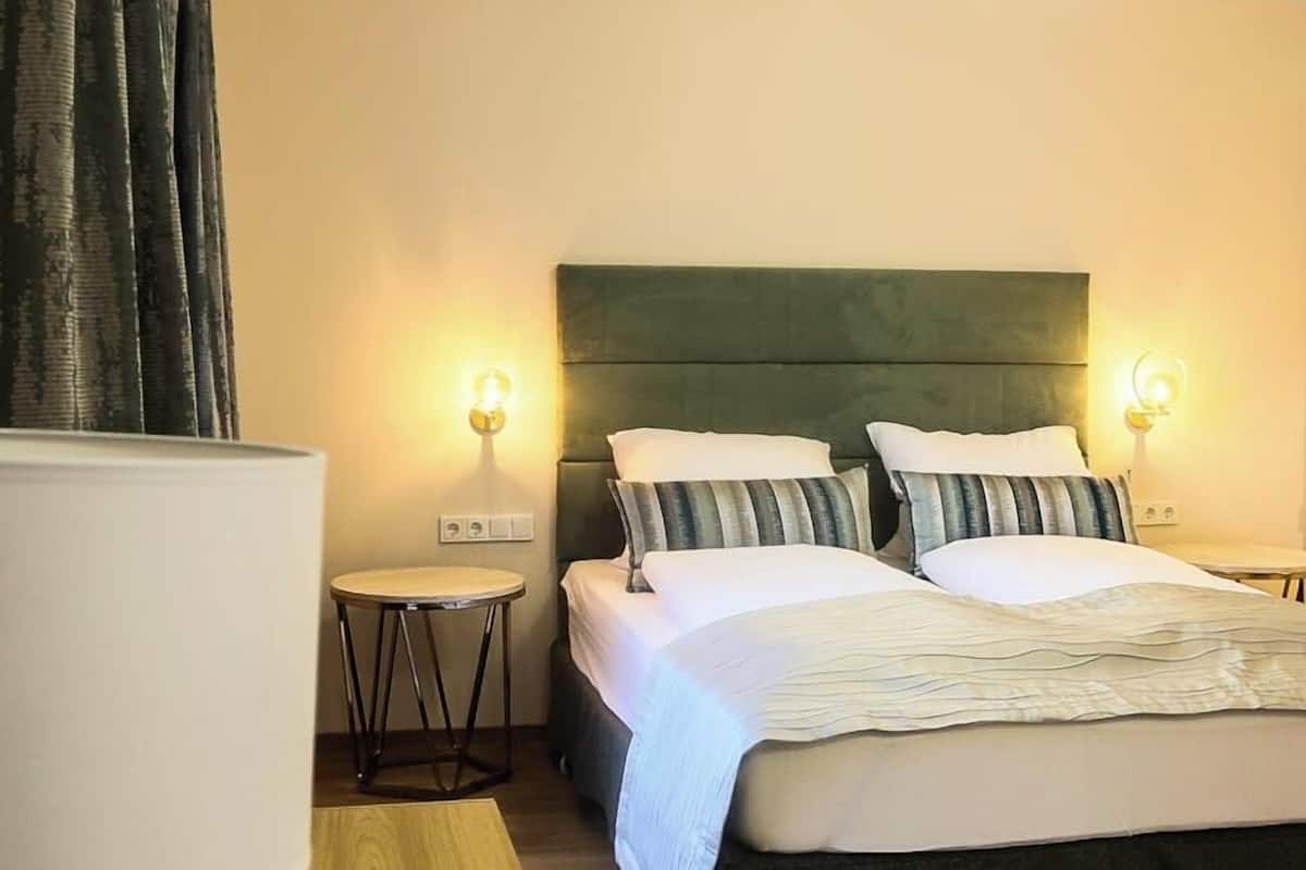 Una habitación de hotel con una cama, lámparas de noche, una mesita y una silla.