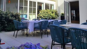 A building with a red-tiled roof, large windows, and a patio area with blue chairs and a table. - Hotel Lutz (Rain)