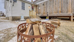 A rustic house with a wooden deck, a metal fire pit with logs, and a satellite dish.