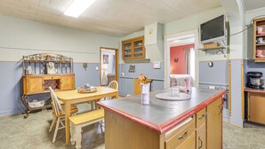 A kitchen with a wooden table, chairs, a countertop, and a television mounted on the wall.