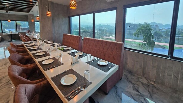 A dining area with a long table set for a meal, large windows with a city view, and an air conditioning unit on the wall. - SC Hotel (Papumpare)