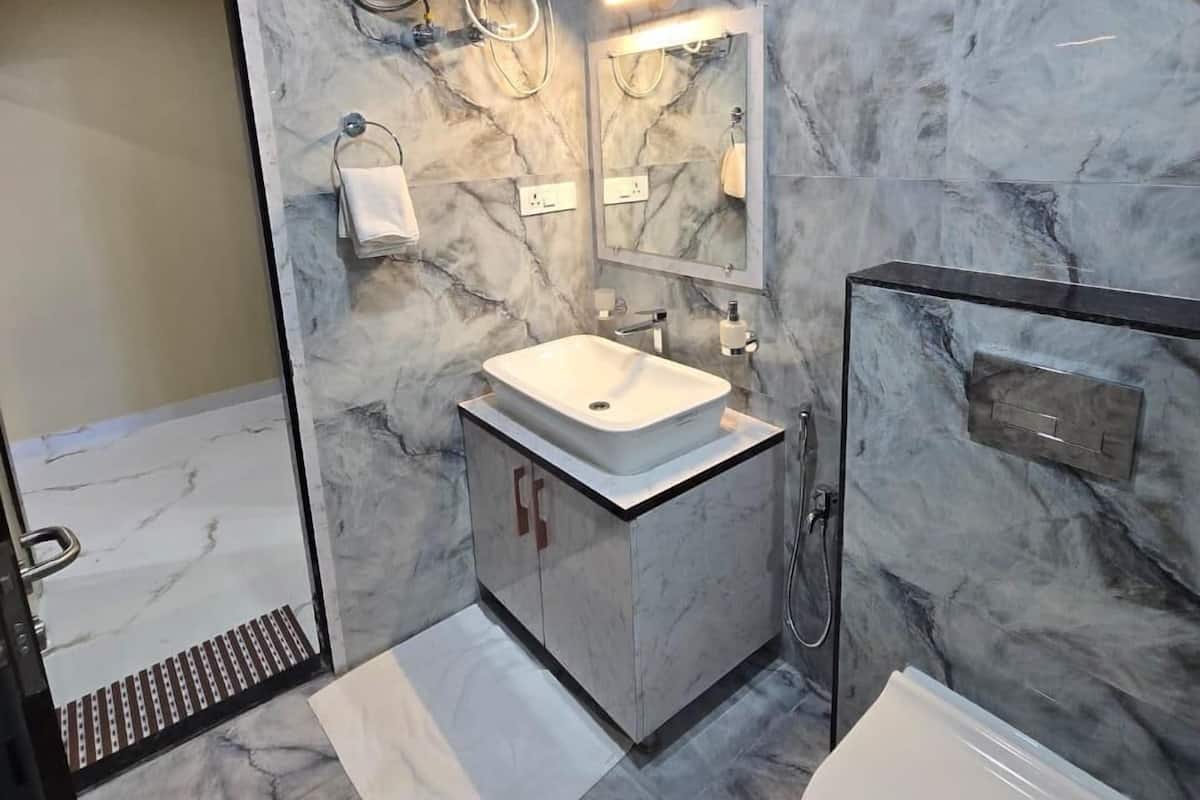 A bathroom with a marble floor, a white sink, a mirror, a toilet, and a shower area.