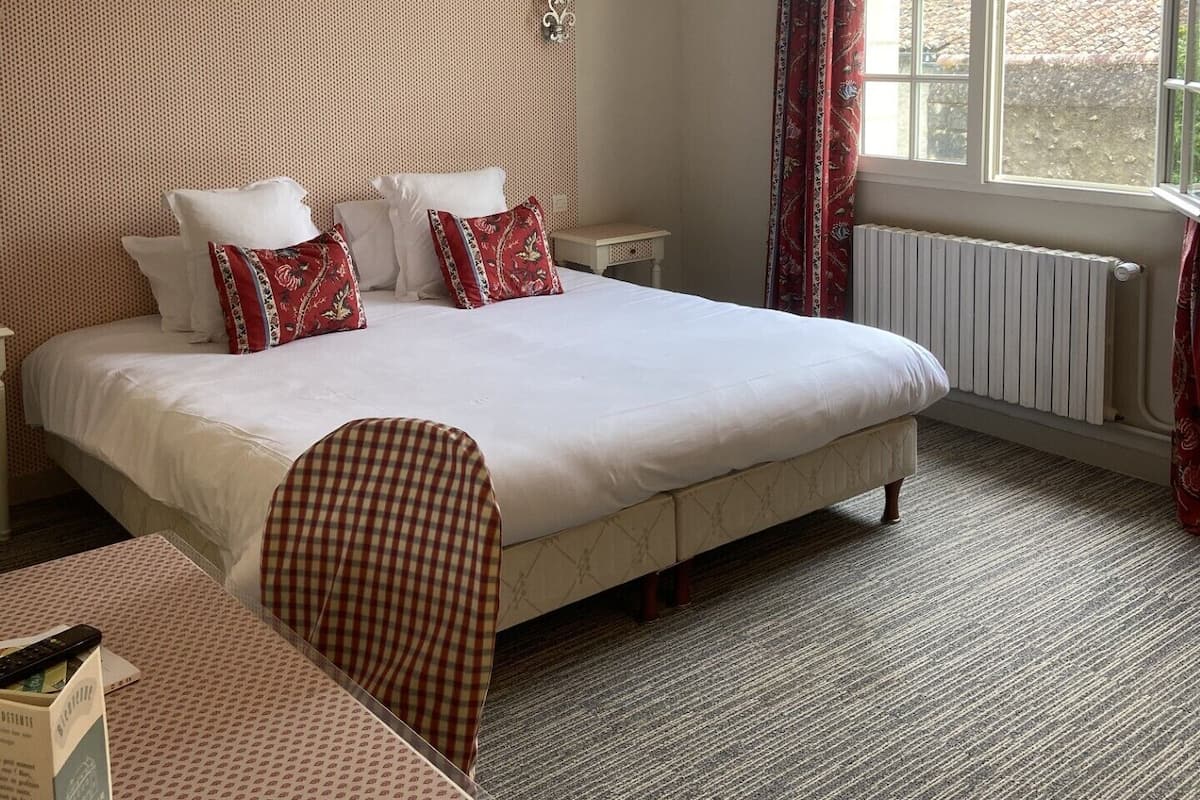 Et hotelværelse med en stor seng, et skrivebord, en lampe og et vindue med udsigt til bygninger.