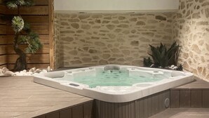 A hot tub in a spa area with a stone wall backdrop and wooden paneling.